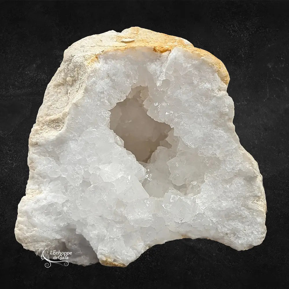 Cavité centrale d'une géode de quartz blanc avec amas de cristaux scintillants et croûte ocre sur fond noir.