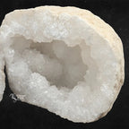 Zoom sur les cristaux intérieurs d'une géode de quartz blanc, texture rocheuse beige en bordure.