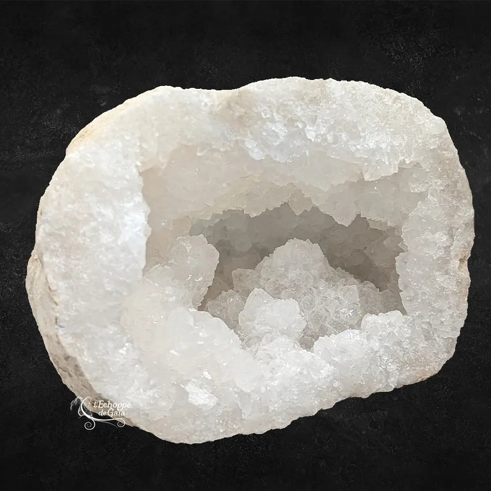Gros plan sur une géode de quartz blanc montrant une cavité remplie de cristaux scintillants sur fond noir.