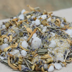 Gros plan d’un mélange d’encens et de plantes séchées, avec cristaux blancs, lamelles végétales et fleurs de lavande sur un tissu beige.
