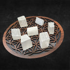Plusieurs morceaux de sélénite brute de forme rectangulaire, d'un blanc pur et fibreux, disposés sur une fleur de vie en bois sur fond noir.