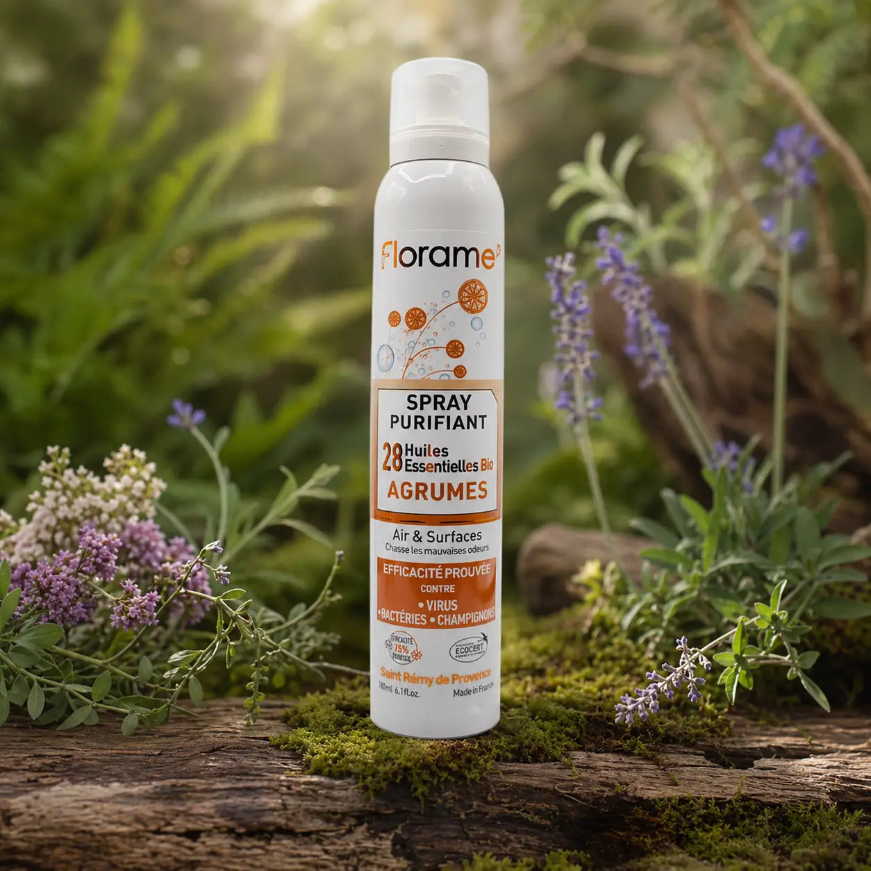 Flacon de spray purifiant bio Florame aux agrumes posé sur une écorce moussue, entouré de fleurs sauvages violettes et blanches dans une lumière naturelle.