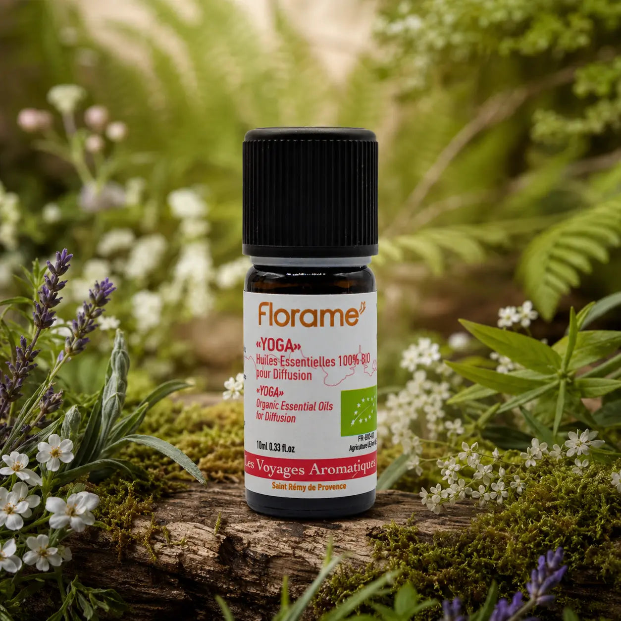 Flacon d'huile essentielle Florame Yoga 10ml posé sur une écorce moussue, entouré de lavande sauvage et de petites fleurs blanches printanières.