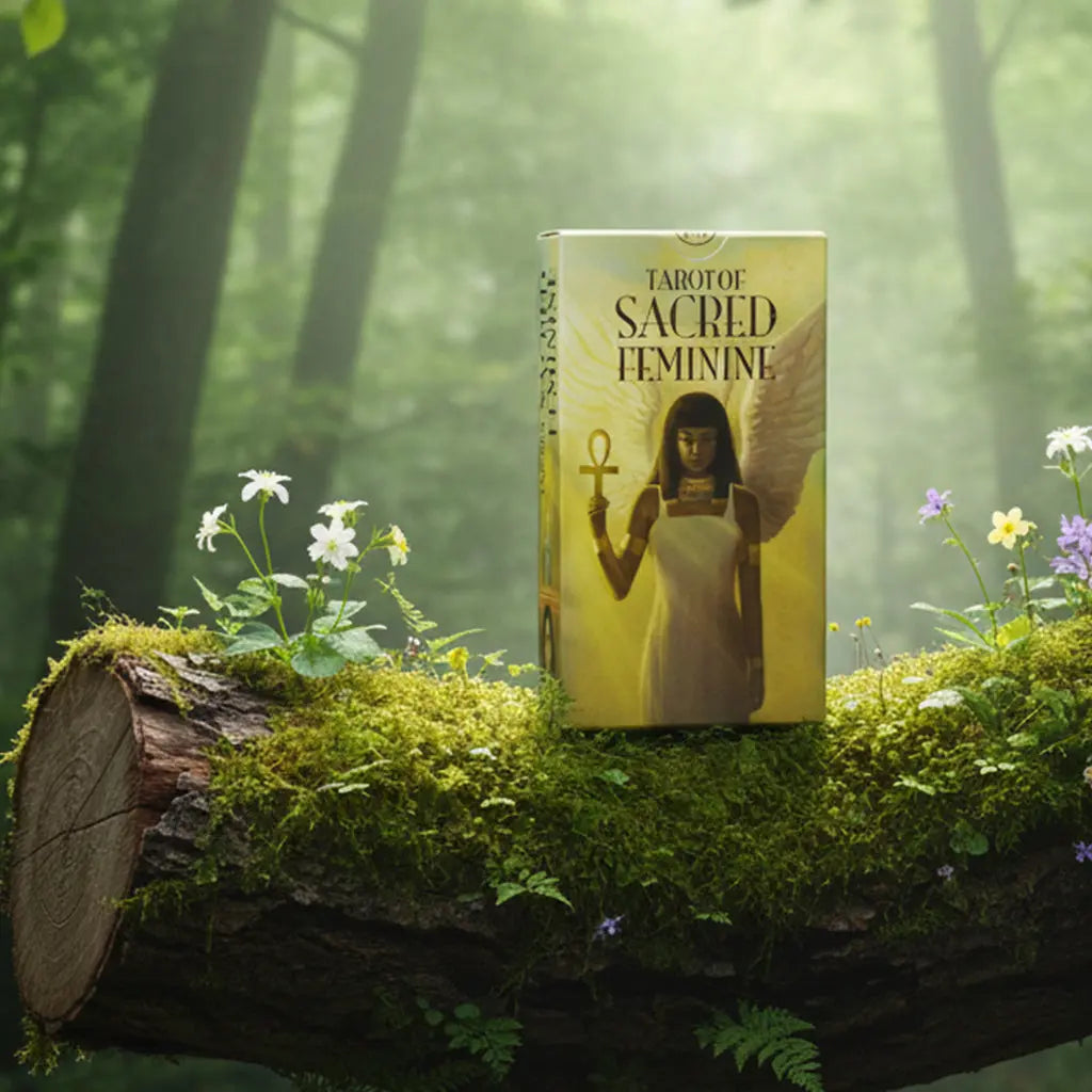 Boîte jaune dorée Tarot Of Sacred Feminine de Lo Scarabeo posée sur une souche, illustrée d'une déesse égyptienne ailée tenant un ankh.